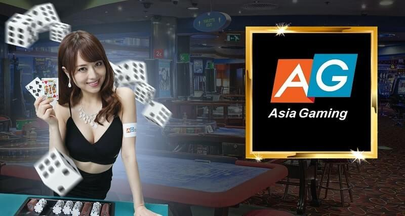 แบนเนอร์โปรโมท asia gaimnig แสดงโลโก้ AG และคำว่า Asia Gaming; ฝั่งขวาเป็นกรอบโลโก้สีทองขนาดใหญ่ ทางซ้ายมีผู้หญิงสวมชุดดำถือไพ่อยู่บนโต๊ะเกม พร้อมชิปและลูกเต๋าลอยอยู่ พื้นหลังเป็นบรรยากาศคาสิโนมีโต๊ะเกม สล็อตแมชชีน และแสงไฟให้ความรู้สึกคาสิโนสด